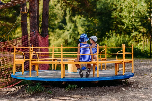 Petits enfants en chapeaux d'été et t-shirts assis sur un grand carrousel de fer dans le parc — Photo