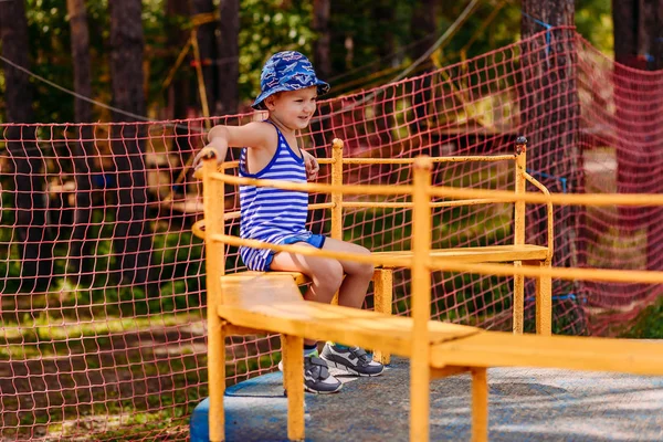 Niño caucásico sonriente de cinco años en un sombrero montado en un carrusel infantil grande en un parque de verano —  Fotos de Stock