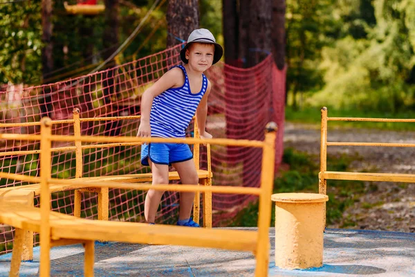 En sjuårig glad pojke i en randig t-shirt och hatt Rider en gul barnens karusell på sommaren. — Stockfoto