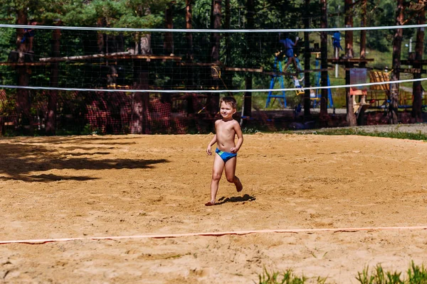 Четырехлетний загорелый ребенок в плавках играет в пляжный волейбол на песке — стоковое фото