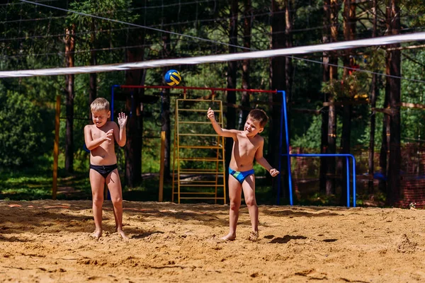 Tanned sports Caucasoid boys in swimming trunks play beach volleyball in the summer — Stock Photo, Image