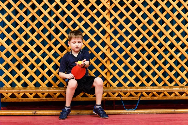 Семилетний ребенок сидит на скамейке с теннисной ракеткой — стоковое фото