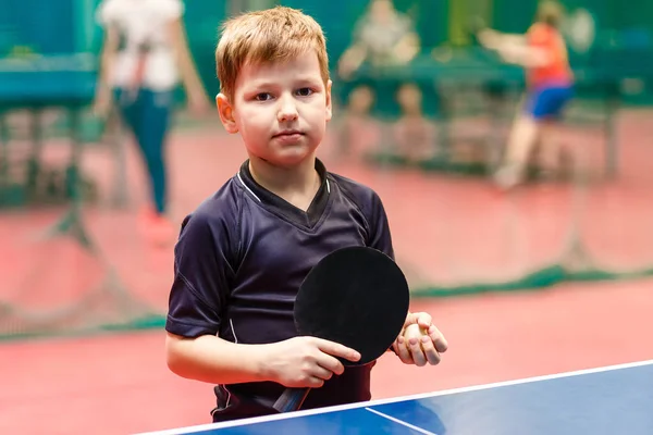 Ребенок теннисист стоит у теннисного стола с ракеткой и мячом в руках — стоковое фото