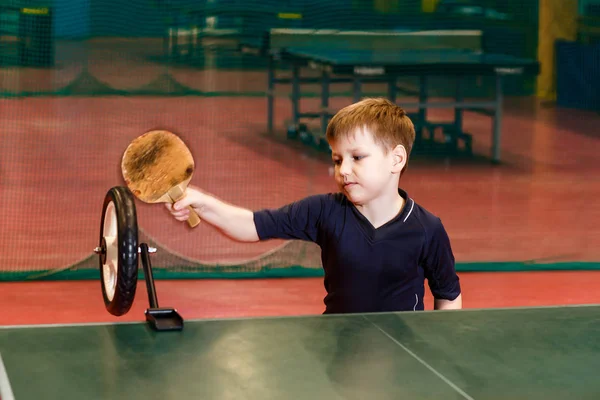 Семилетний ребенок в серой форме поезда забастовки в настольном теннисе с помощью робота на столе — стоковое фото
