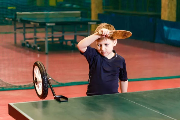 Семилетний ребенок в спортивной форме учится играть в настольный теннис с помощью тренажера — стоковое фото