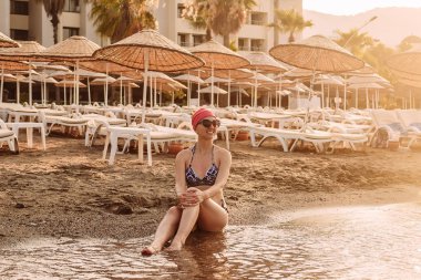 plajda oturan bir mayo içinde gülümseyen kadın
