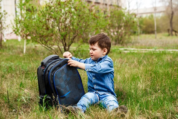 잔디에 앉아 있는 큰 배낭을 여는 어린 소년 — 스톡 사진