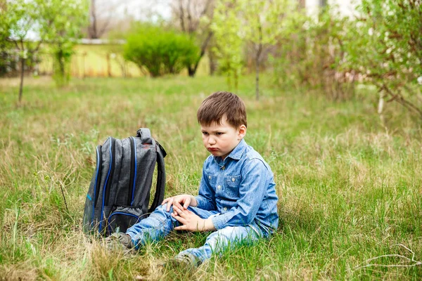 Грустный маленький мальчик и большой рюкзак на зеленой траве — стоковое фото