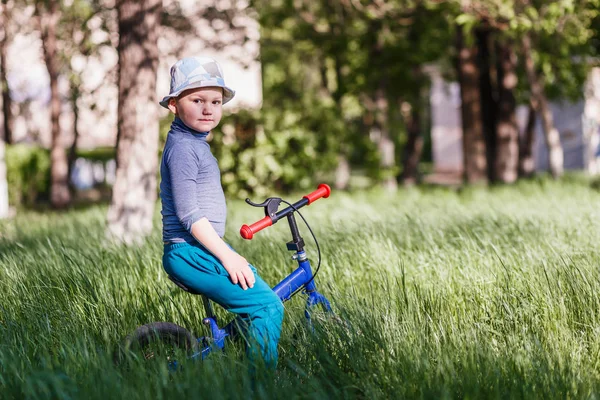 Park'taki yeşil çimenlerde koşucunun üzerinde oturan şapkalı dört yaşındaki çocuk — Stok fotoğraf