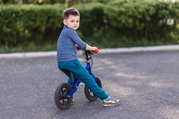 Четырехлетний милый мальчик в кроссовках оглядывается назад. Дети и спорт. Дети и лето. Велосипед без педалей — стоковое фото