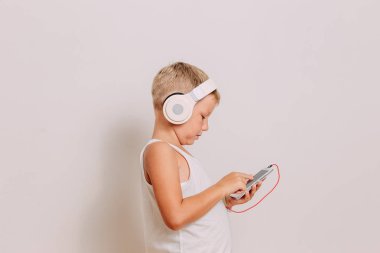elinde bir akıllı telefon ve büyük beyaz kulaklık ile yedi yaşındaki sarışın çocuk