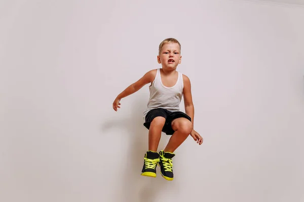 Menino caucasiano de sete anos de idade em uniforme de basquete pulando alto no fundo branco — Fotografia de Stock