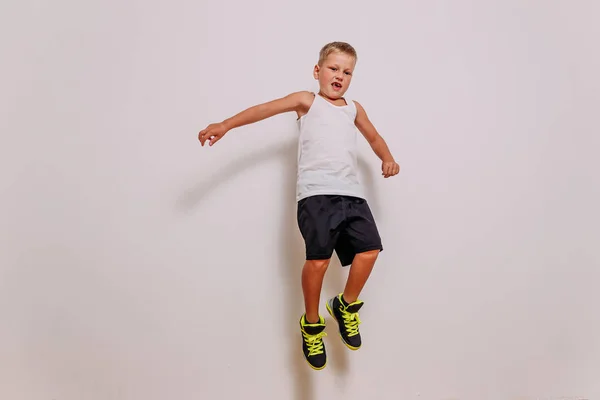 Menino de sete anos de idade em uniforme de basquete pulando alto no fundo branco — Fotografia de Stock