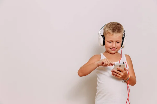 Cute siedmioletni chłopiec ze słuchawkami i monitorów z telefonem w dłoniach. Nowoczesna technologia — Zdjęcie stockowe