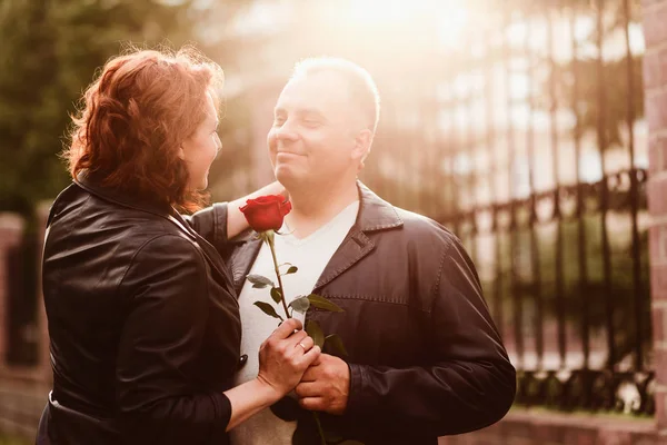 Starší muž dává ženě červenou růži. Šťastný ženatý pár. Lidé v podsvícení — Stock fotografie