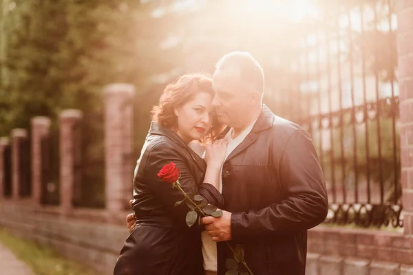 Ein älterer Mann überreicht einer Frau eine rote Rose. die Frau mit den roten Lippen legte ihren Kopf auf die Schulter des Mannes. glückliches Ehepaar. — Stockfoto