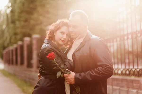 Ein älterer Mann überreicht einer Frau eine rote Rose. Eine Frau mit roten Lippen umarmt einen Mann. glückliches Ehepaar. Menschen im Gegenlicht — Stockfoto