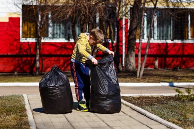 yedi yaşındaki çocuk ilkbaharda büyük bir plastik torba içinde çöp kaldırır