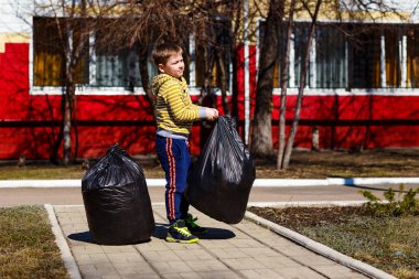 Yedi yaşındaki çocuk ilkbaharda enkaz alanını temizler. Büyük siyah plastik torbalar