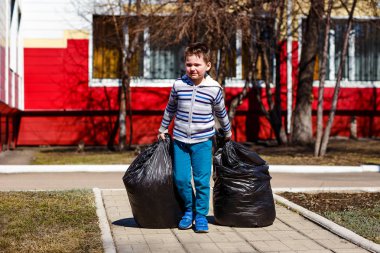 Beş yaşındaki bir çocuk çöp büyük ağır plastik torbalar taşır. Bölgenin temizliği