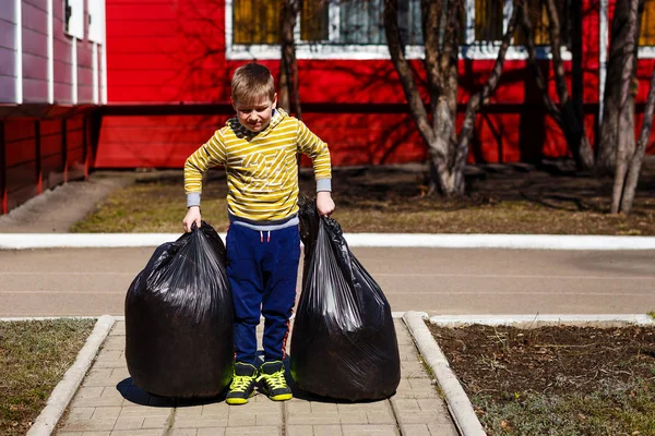 yedi yaşındaki çocuk çöp büyük plastik torbalar taşır.