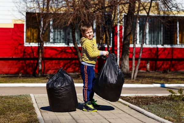 Bambino di sette anni e la pulizia della zona dalla spazzatura in primavera. Grandi borse nere — Foto Stock