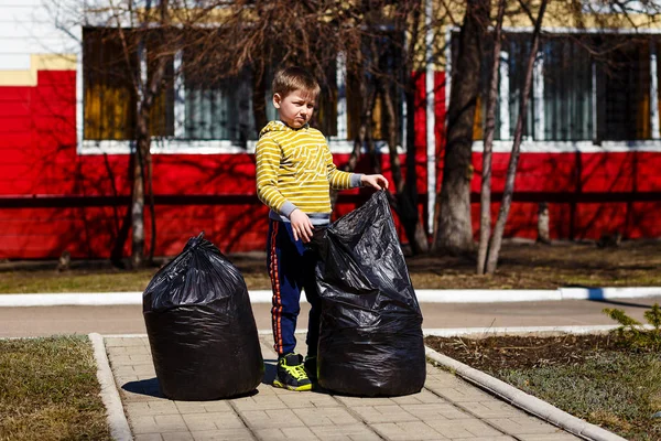 Pulizia della natura dalla spazzatura. Ragazzo e sacchetti di plastica nera di spazzatura in primavera — Foto Stock