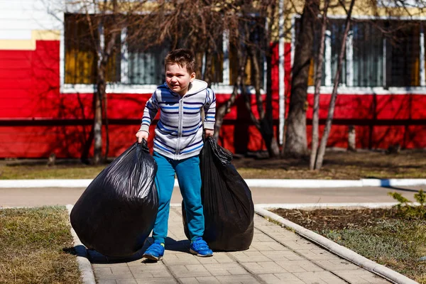 Un bambino di cinque anni trasporta grandi sacchetti di plastica nera di spazzatura . — Foto Stock