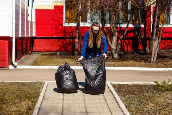 30-летняя женщина собирает мусор в больших пластиковых пакетах. Уход за окружающей средой, очистка территории, утилизация отходов — стоковое фото