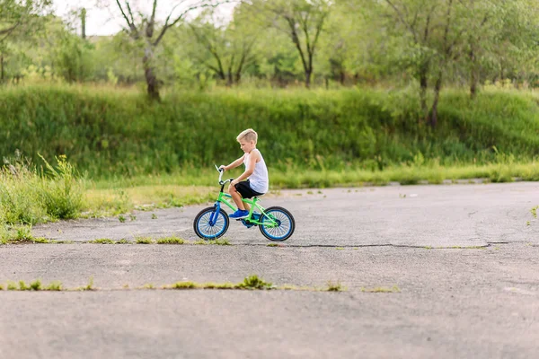 Seven-year-old boy in a white t-shirt rides a children's blue bike in the summer — Stock Photo, Image