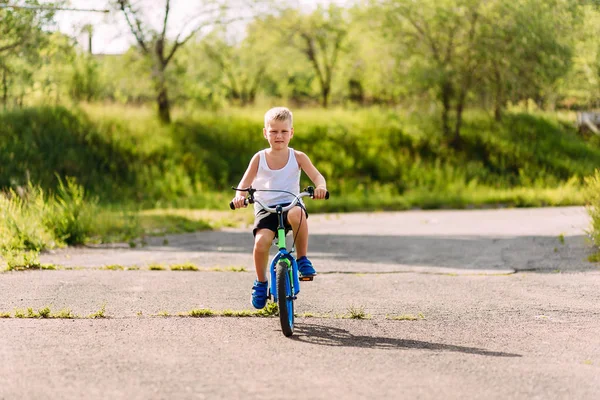 Seven-year-old boy in a white t-shirt rides a children's blue bi — Stock Photo, Image