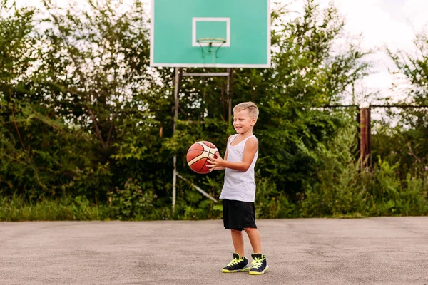 basketbol üniforması neşeli bir yedi yaşındaki çocuk yaz aylarında açık bir basketbol sahasında bir top ile oynar.
