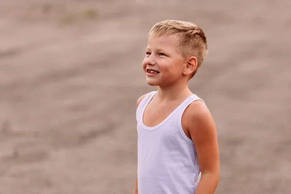 Улыбающийся ребенок в белой хлопчатобумажной футболке на открытом воздухе в размытое лето — стоковое фото