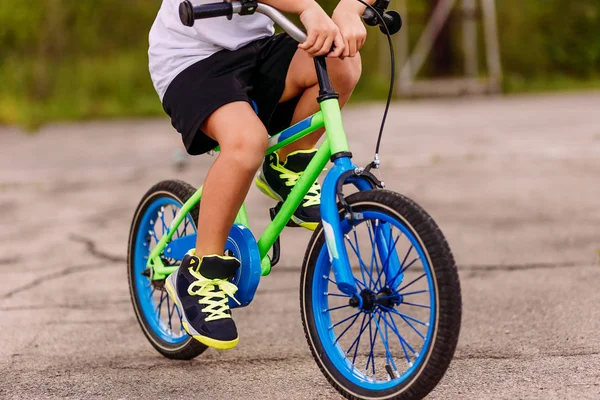 a child in sneakers pedaling a two-Wheeler on the asphalt in the summer. only feet on the pedals of the bike