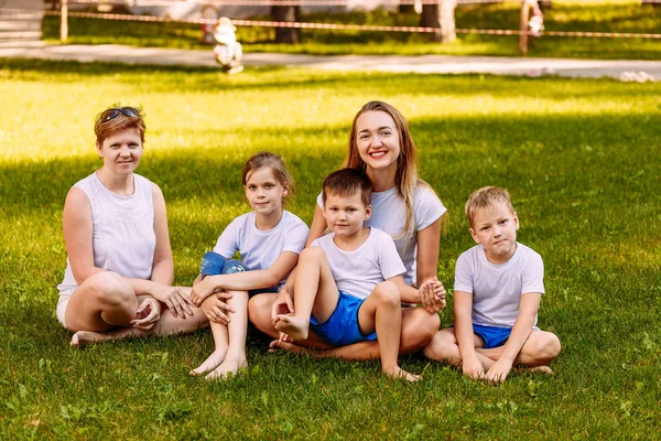 Two women and three children sit on green grass — Stock Photo, Image