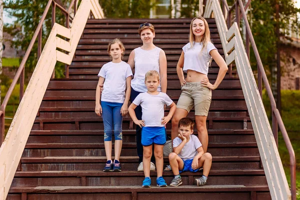 Dos mujeres y tres niños en pleno crecimiento en camisetas blancas de pie en una escalera en el verano — Foto de Stock