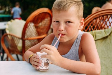 yedi yaşındaki sarışın sevimli bebek açık havada bir yaz restoranda bir tüp suyu içme
