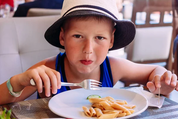 Шестилетний ребенок в шляпе ест макароны — стоковое фото