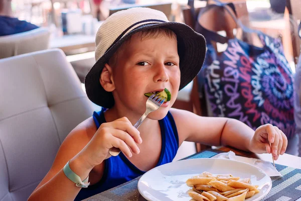 Шестилетний ребенок в шляпе ест макароны в летнем кафе — стоковое фото