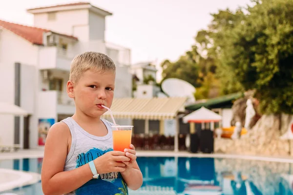 7-летний загорелый блондин пьет апельсиновый безалкогольный коктейль из трубки на открытом воздухе — стоковое фото
