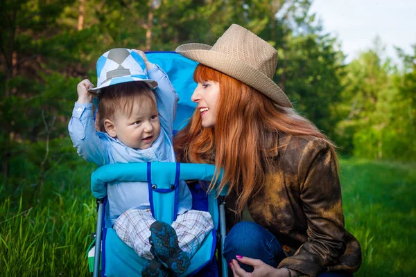 a red-haired fifty-year-old smiling woman in a hat and a two-year-old boy in the summer in the woods.