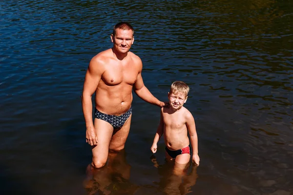 a tanned man and a seven-year-old child swim in the pond in the summer.