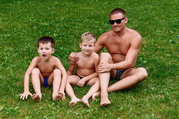幸せな父親と2人の子供が草の上に座る — ストック写真