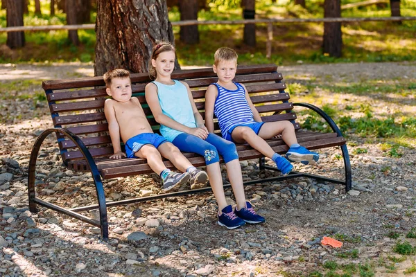 Två pojkar och en tjej som sitter på en bänk på sommaren. Tre barn — Stockfoto