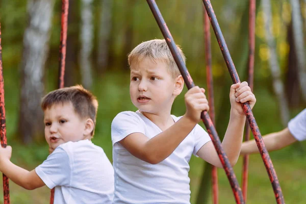 Two boys in white t-shirts ride a swing in the summer — 스톡 사진