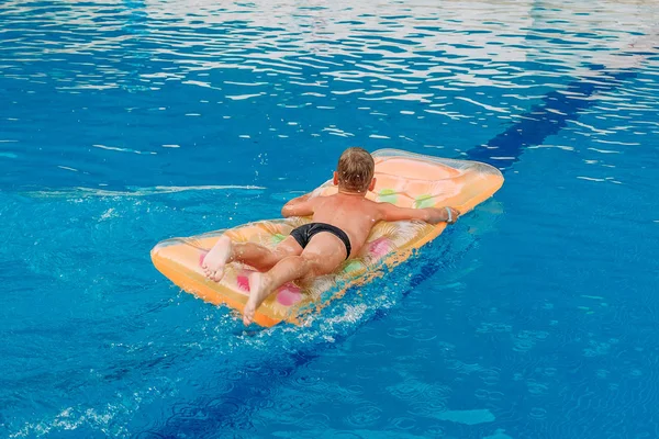 seven-year-old child swims on an inflatable mattress in the outdoor pool in the summer.