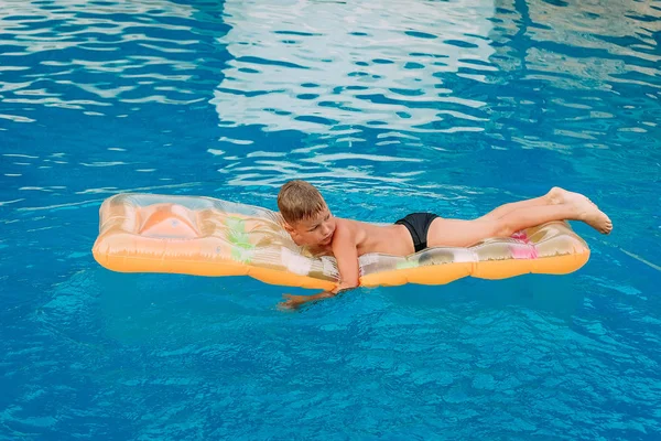 Εφτά ετών μαυρισμένο παιδί κολυμπάει σε ένα φουσκωτό στρώμα στην εξωτερική πισίνα . — Φωτογραφία Αρχείου