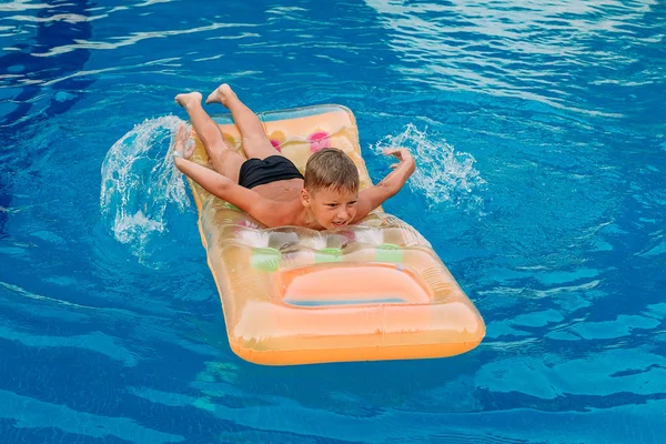Ein gebräuntes siebenjähriges Kind schwimmt auf einer aufblasbaren Matratze im Freibad. Rudernde Hände im Wasser — Stockfoto
