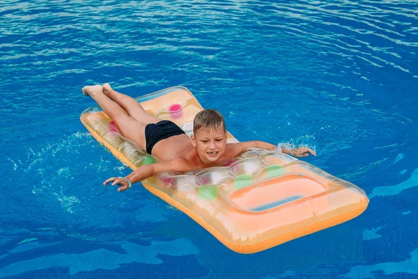 Щасливий семирічний хлопчик лежить на повітряному матраці у відкритому басейні влітку. Блакитна вода — стокове фото