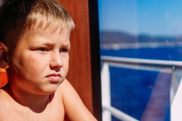 Серьезный семилетний мальчик смотрит в окно корабля — стоковое фото
